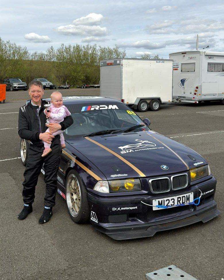 Rob with his daughter and a trophy, beside RDM's E36 race car